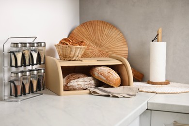 Photo of Wooden bread basket, freshly baked loaves and croissants on white marble table in kitchen