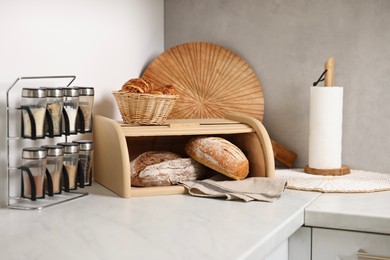 Wooden bread basket, freshly baked loaves and croissants on white marble table in kitchen