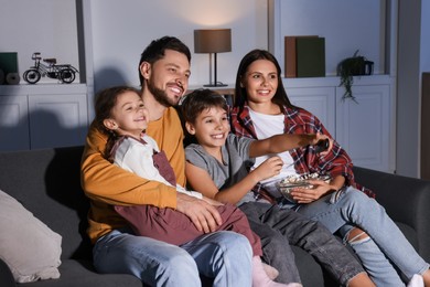 Photo of Happy family watching TV at home in evening. Son changing channels with remote control