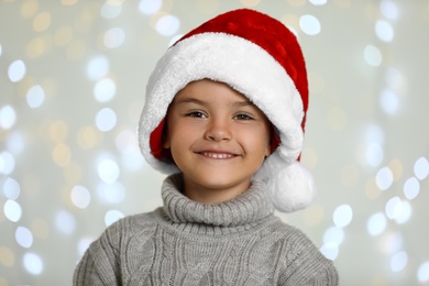 Photo of Happy little child in Santa hat against blurred festive lights. Christmas celebration