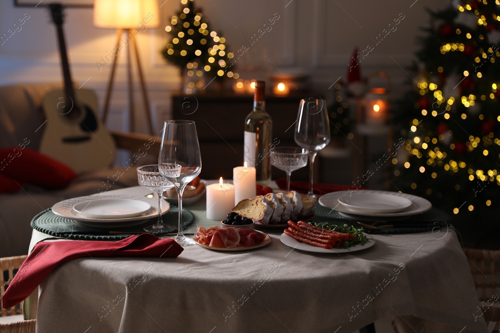 Photo of Christmas table setting with burning candles, appetizers and dishware in room