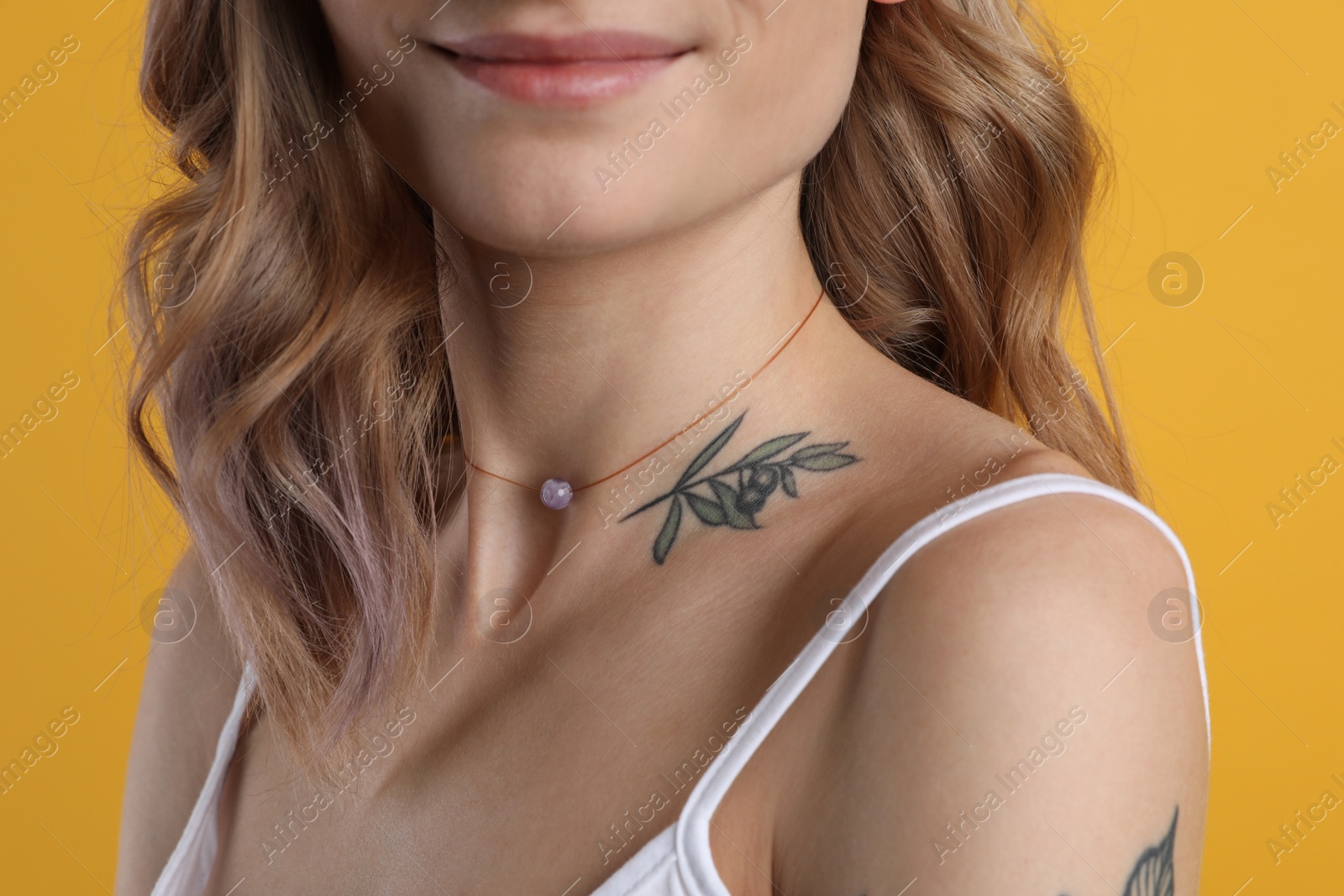 Photo of Beautiful woman with tattoos on body against yellow background, closeup