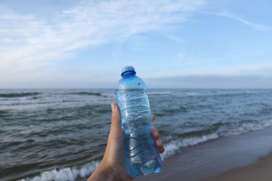 Woman holding plastic bottle with water near sea, closeup