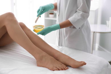 Photo of Woman getting wax epilation of legs in salon, closeup