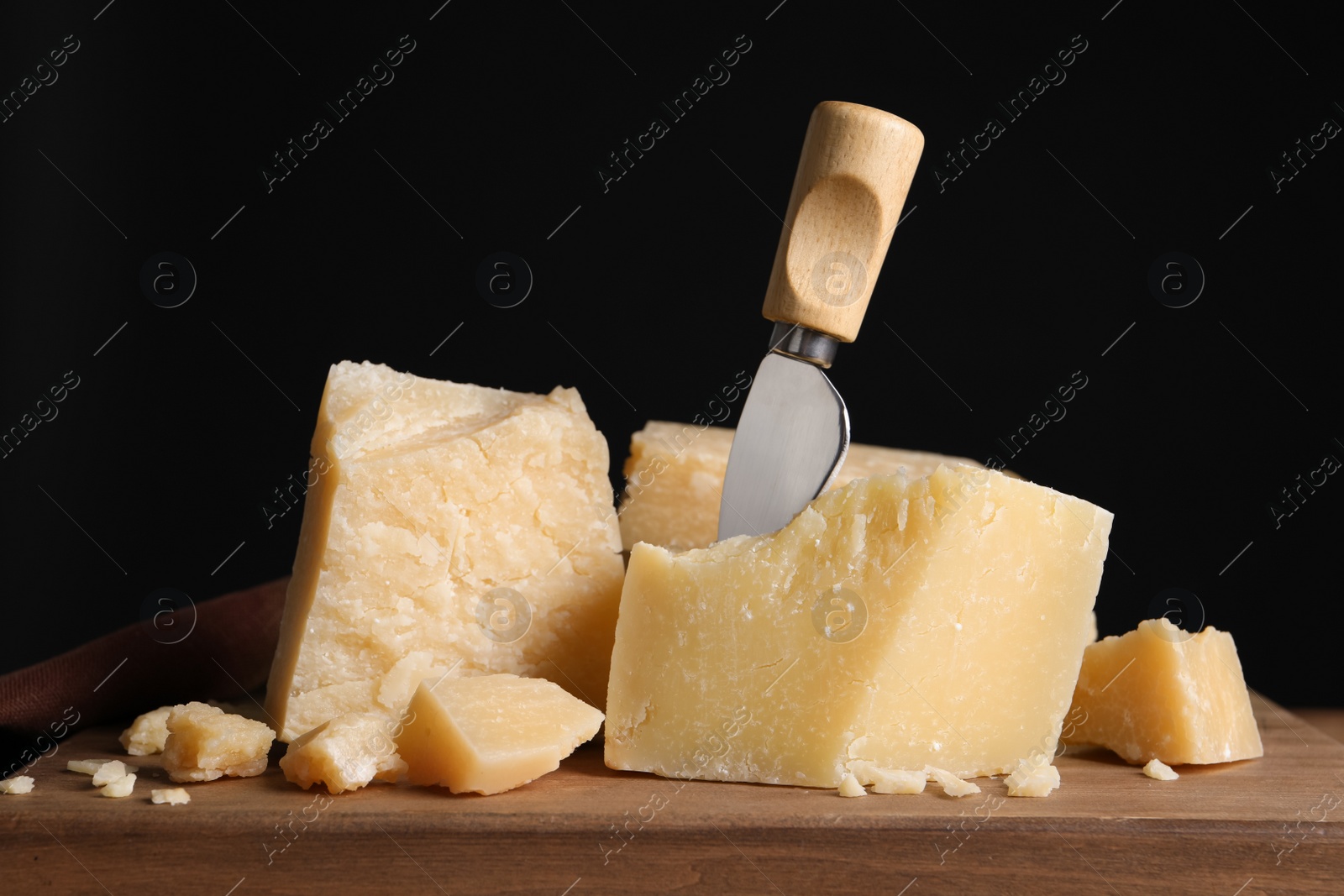 Photo of Parmesan cheese with knife on wooden board, closeup