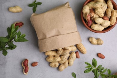 Photo of Paper bag with fresh unpeeled peanuts and leaves on grey table, flat lay