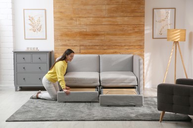 Photo of Young woman unfolding sofa into a bed in room. Modern interior