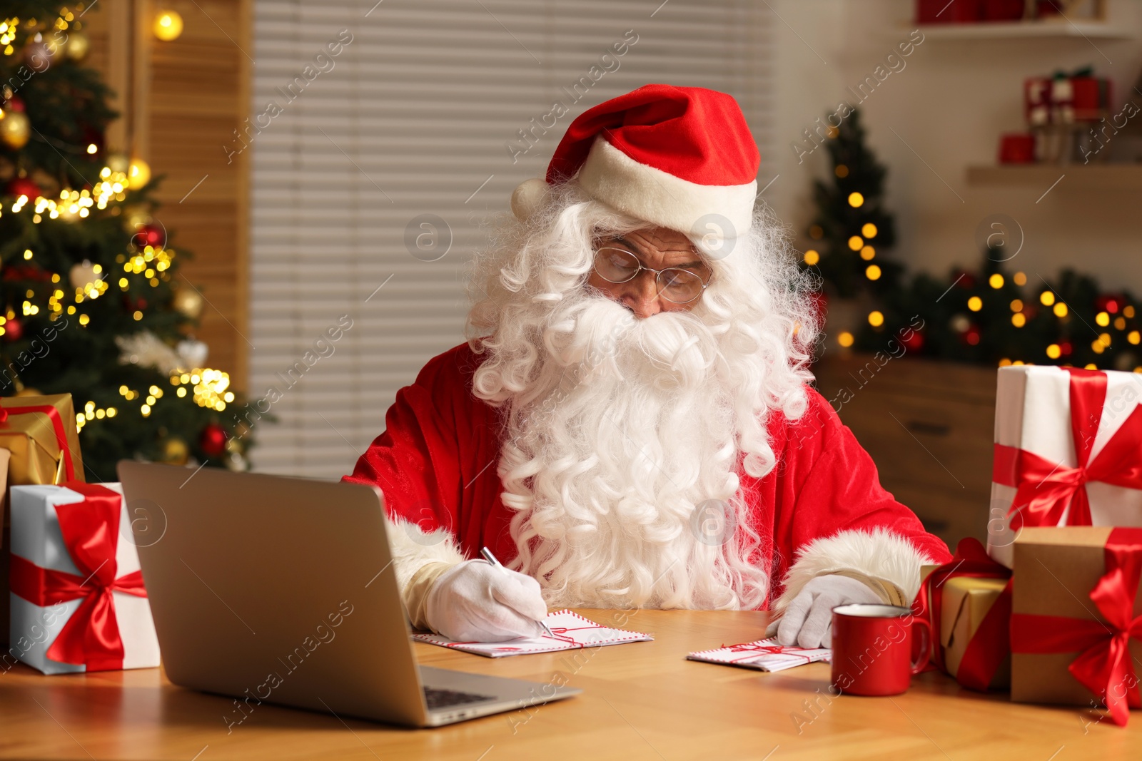 Photo of Santa Claus signing Christmas letters at table in room