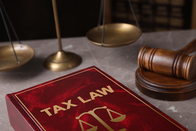 Image of Tax law book and gavel on grey marble table, closeup