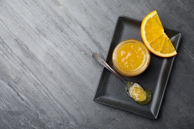 Delicious orange marmalade in jar and spoon on grey table, top view. Space for text