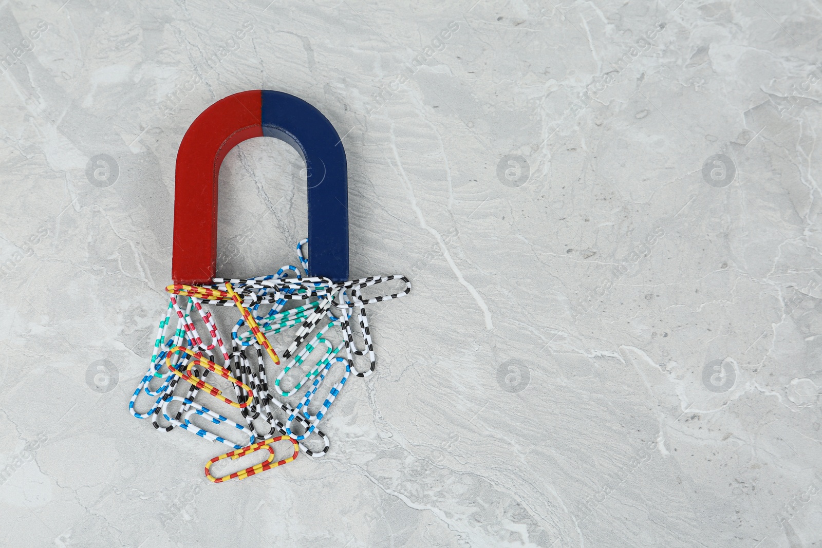 Photo of Magnet attracting paper clips on grey marble table, flat lay. Space for text