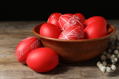 Photo of Wooden bowl with red painted Easter eggs on table