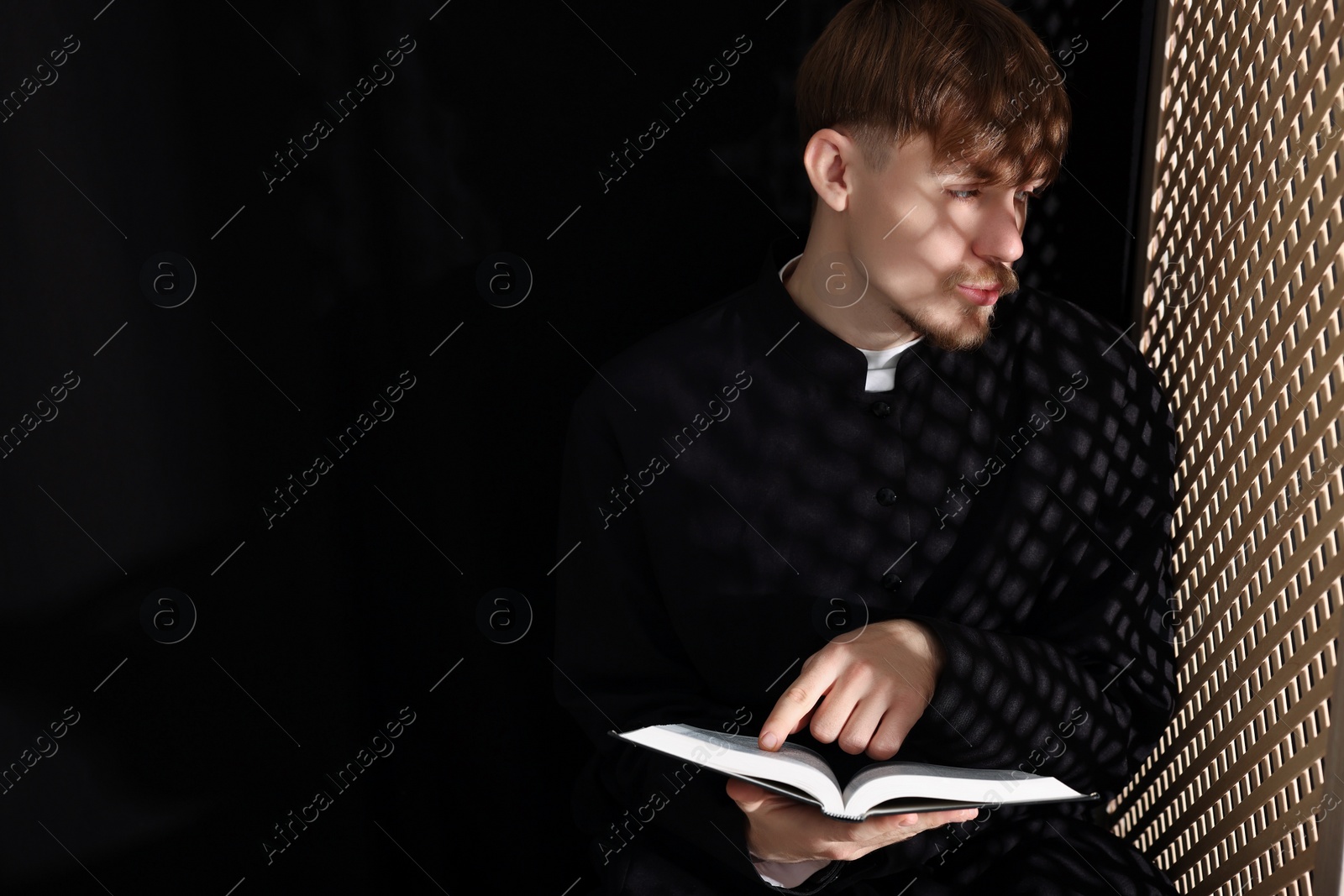 Photo of Catholic priest with Bible talking to parishioner in confessional. Space for text