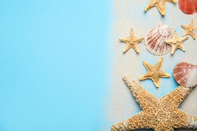 Photo of Beautiful sea stars, shells and sand on light blue background, flat lay. Space for text