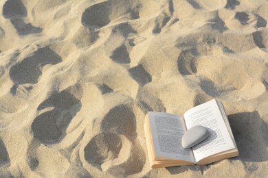 Photo of Open book with stone on sandy beach, above view. Space for text