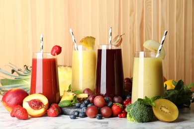 Photo of Glasses of delicious juices and fresh ingredients on white marble table