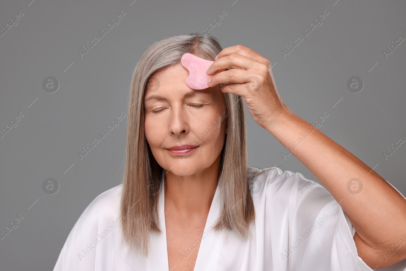 Photo of Woman massaging her face with rose quartz gua sha tool on grey background