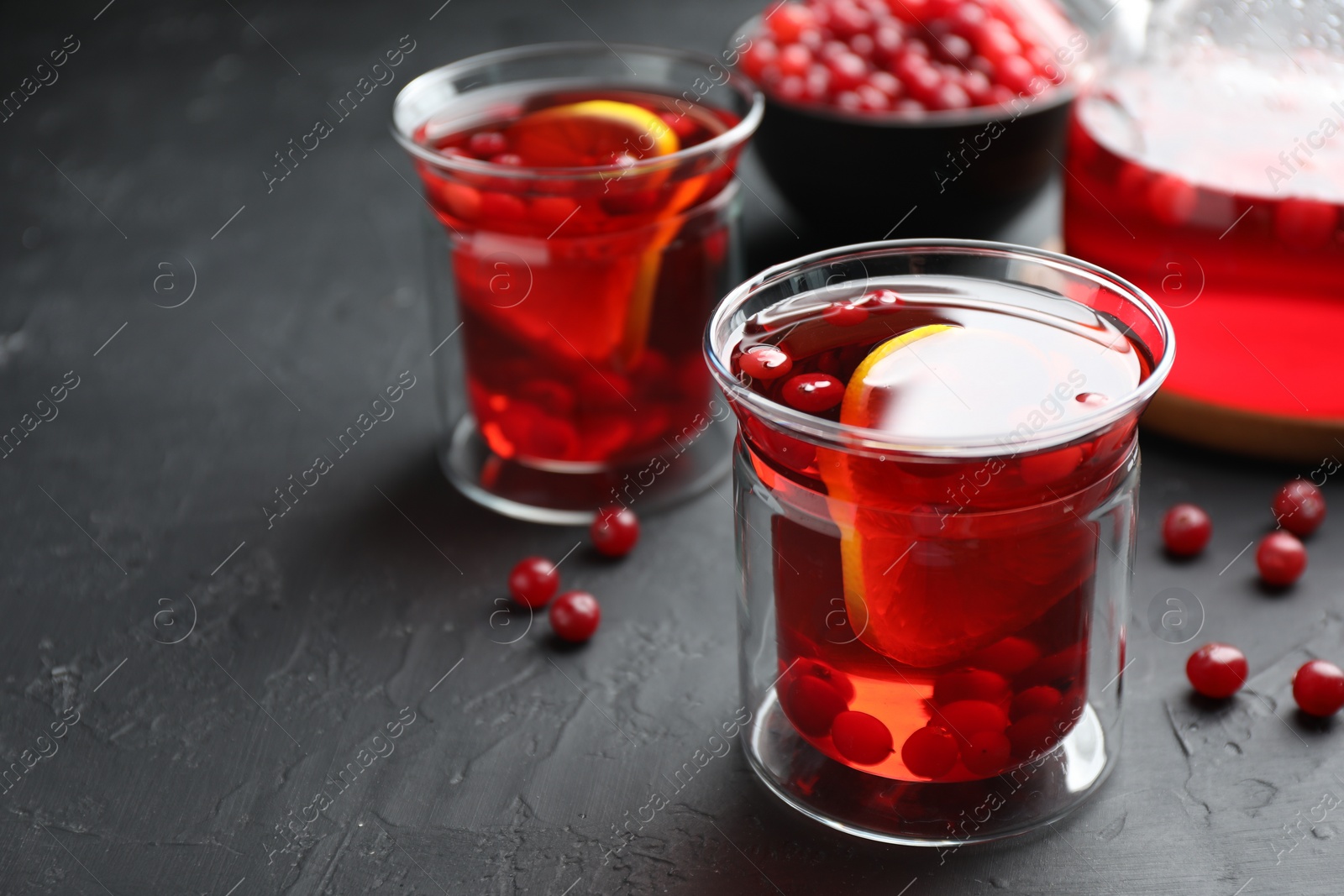 Photo of Tasty hot cranberry tea with lemon and fresh berries in glass on black textured table