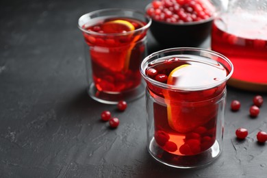 Photo of Tasty hot cranberry tea with lemon and fresh berries in glass on black textured table