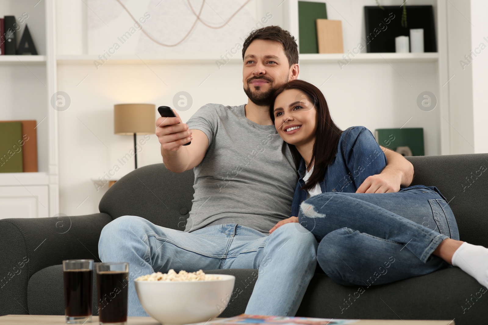 Photo of Happy couple watching show at home. Man changing TV channels with remote control