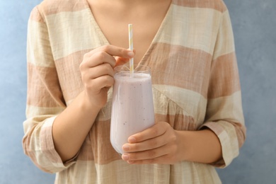 Woman holding fig smoothie on light blue background, closeup