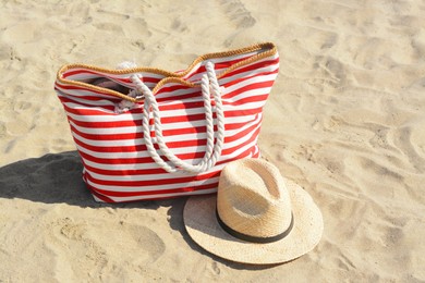 Photo of Stylish striped bag with straw hat on sandy beach