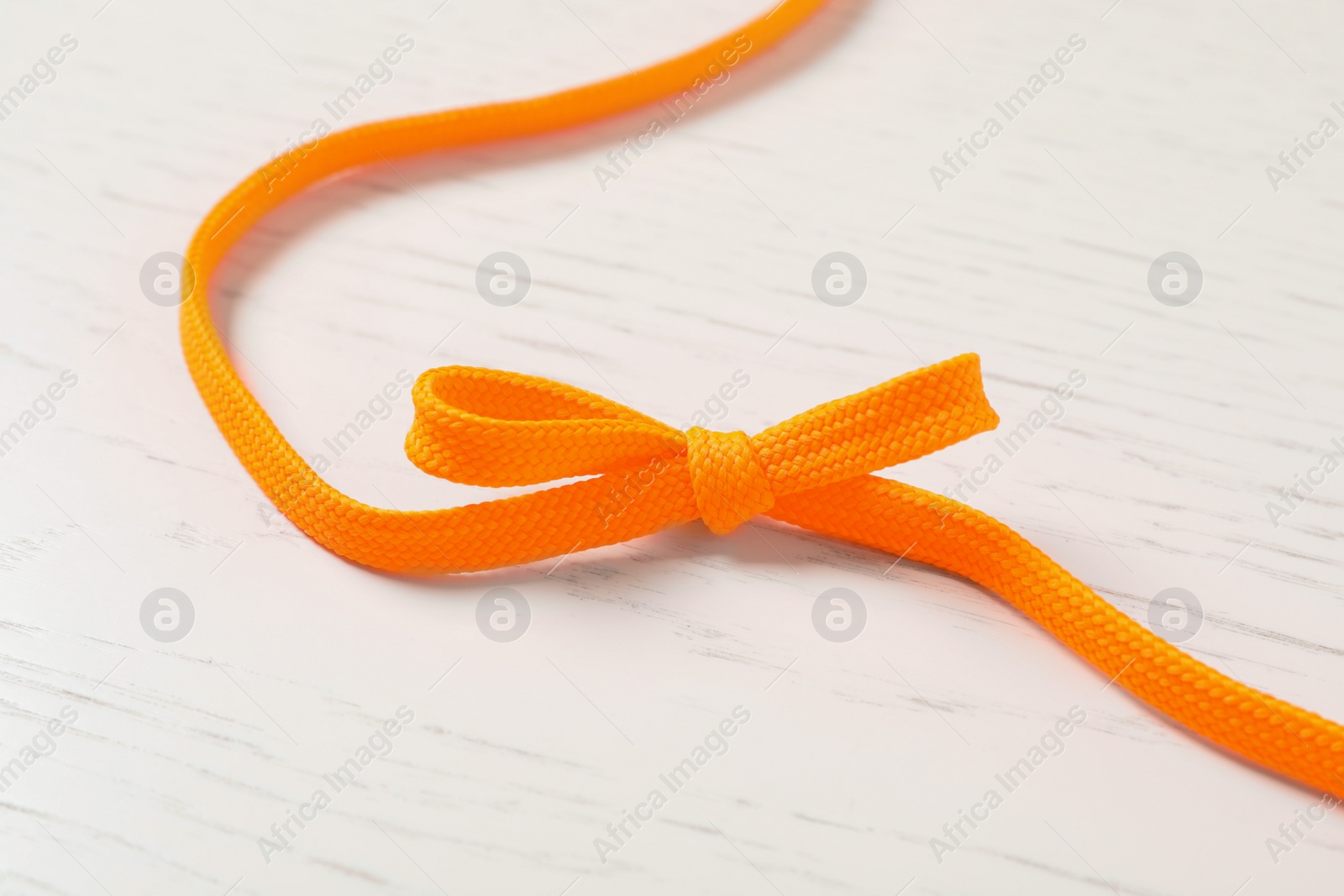 Photo of Orange shoelace on white wooden background. Stylish accessory