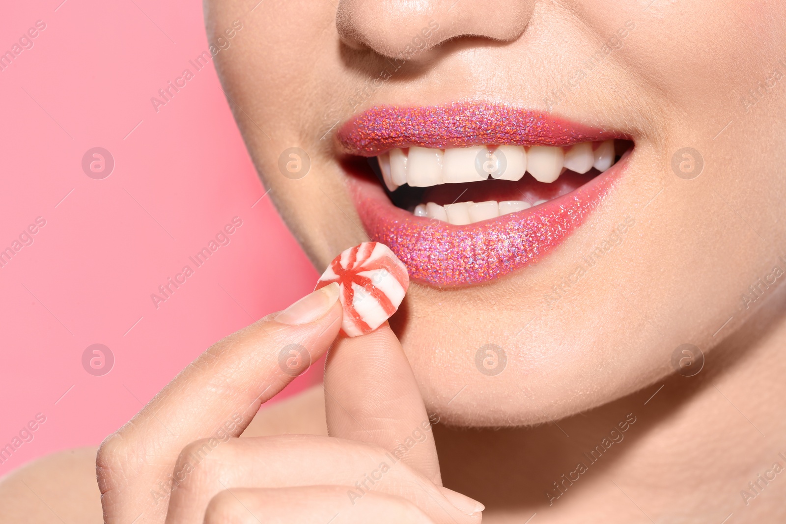 Photo of Beautiful young model with creative makeup holding candy in lips on color background