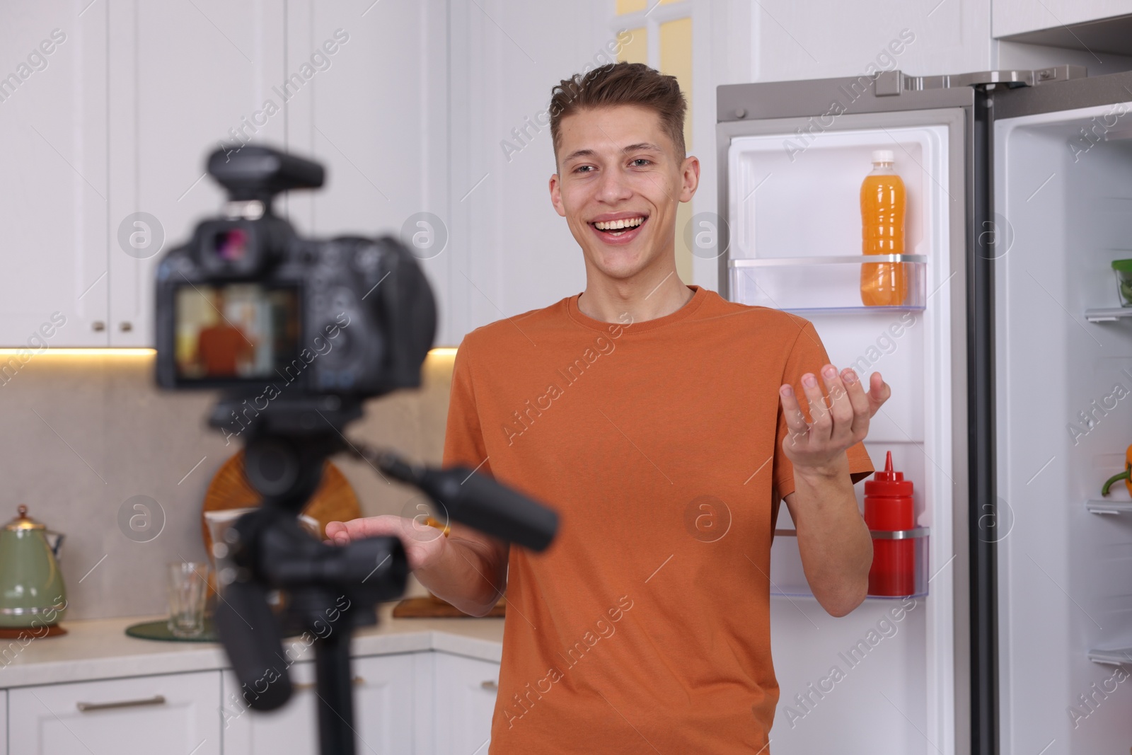 Photo of Smiling food blogger explaining something while recording video in kitchen