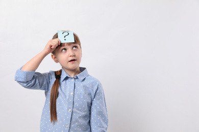 Photo of Emotional girl with question mark sticker on forehead against white background. Space for text