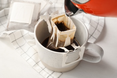 Photo of Pouring hot water into glass cup with drip coffee bag on white wooden table, closeup