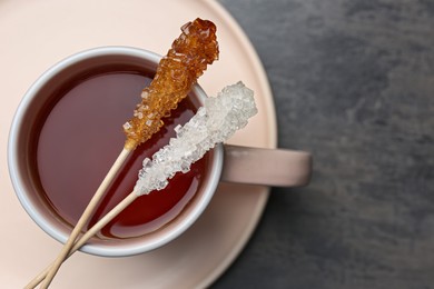 Photo of Sticks with sugar crystals and cup of tea on grey table, top view. Space for text