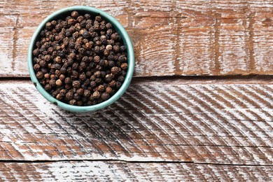 Aromatic spice. Black pepper in bowl on wooden table, top view. Space for text