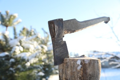 Metal axe in wooden log outdoors on sunny winter day, closeup. Space for text