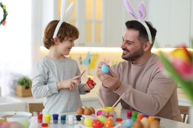 Photo of Easter celebration. Happy father with his little son painting eggs at table in kitchen