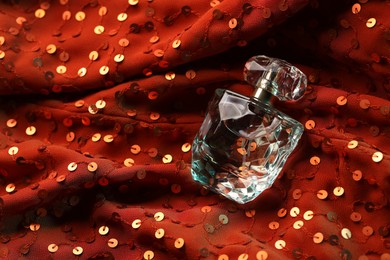 Photo of Luxury perfume in bottle on red fabric with sequins