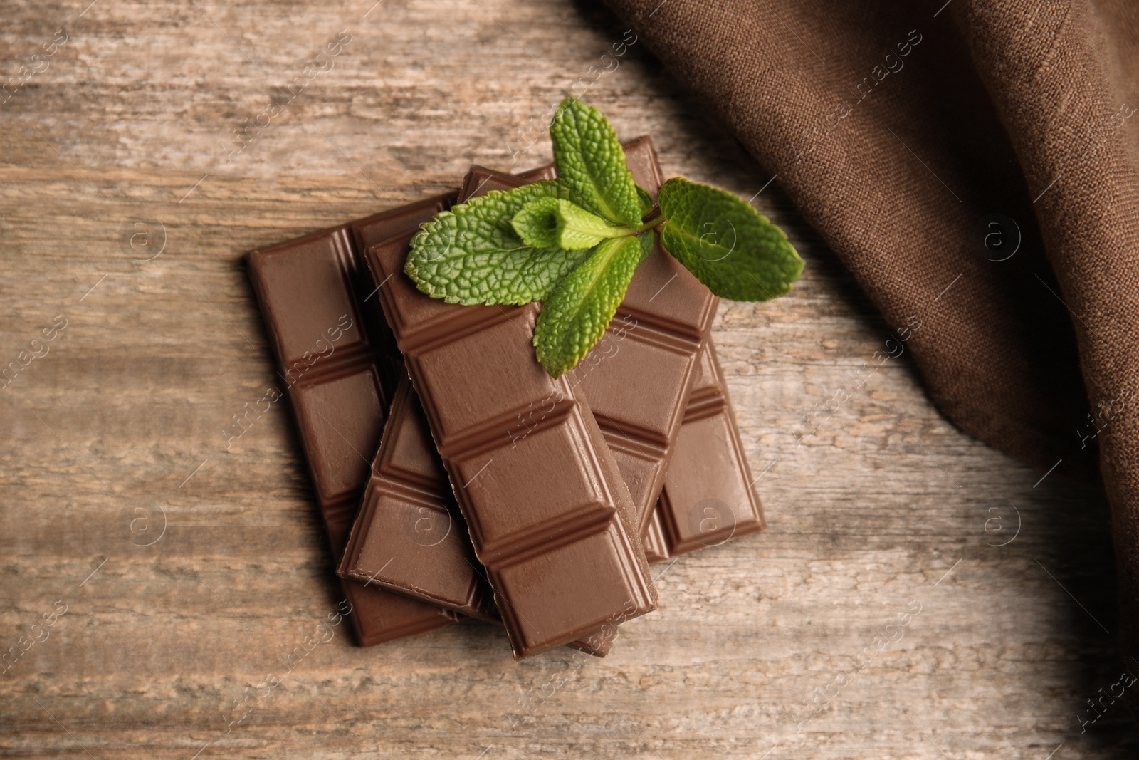 Photo of Tasty milk chocolate pieces with mint on wooden table, top view
