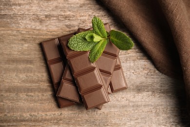 Photo of Tasty milk chocolate pieces with mint on wooden table, top view