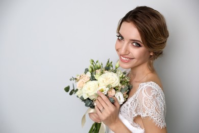 Photo of Young bride with elegant hairstyle holding wedding bouquet on light grey background. Space for text