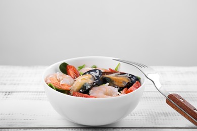 Photo of Bowl of delicious salad with seafood on white wooden table