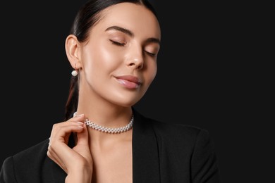 Young woman with elegant pearl jewelry on black background, space for text