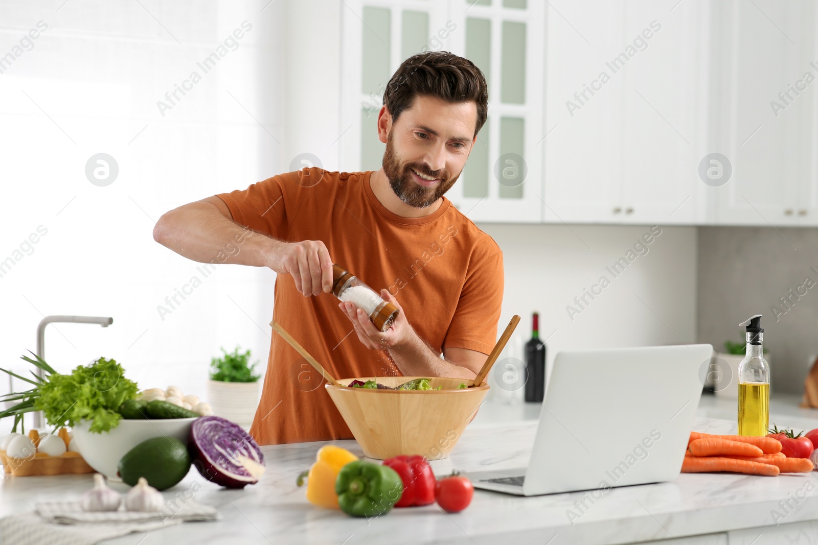 Photo of Man making dinner while watching online cooking course via laptop in kitchen