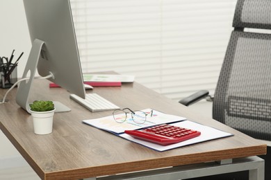 Photo of Calculator, documents, glasses and computer on wooden desk in office