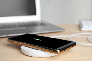 Photo of Mobile phone charging with wireless pad on wooden table, closeup. Space for text