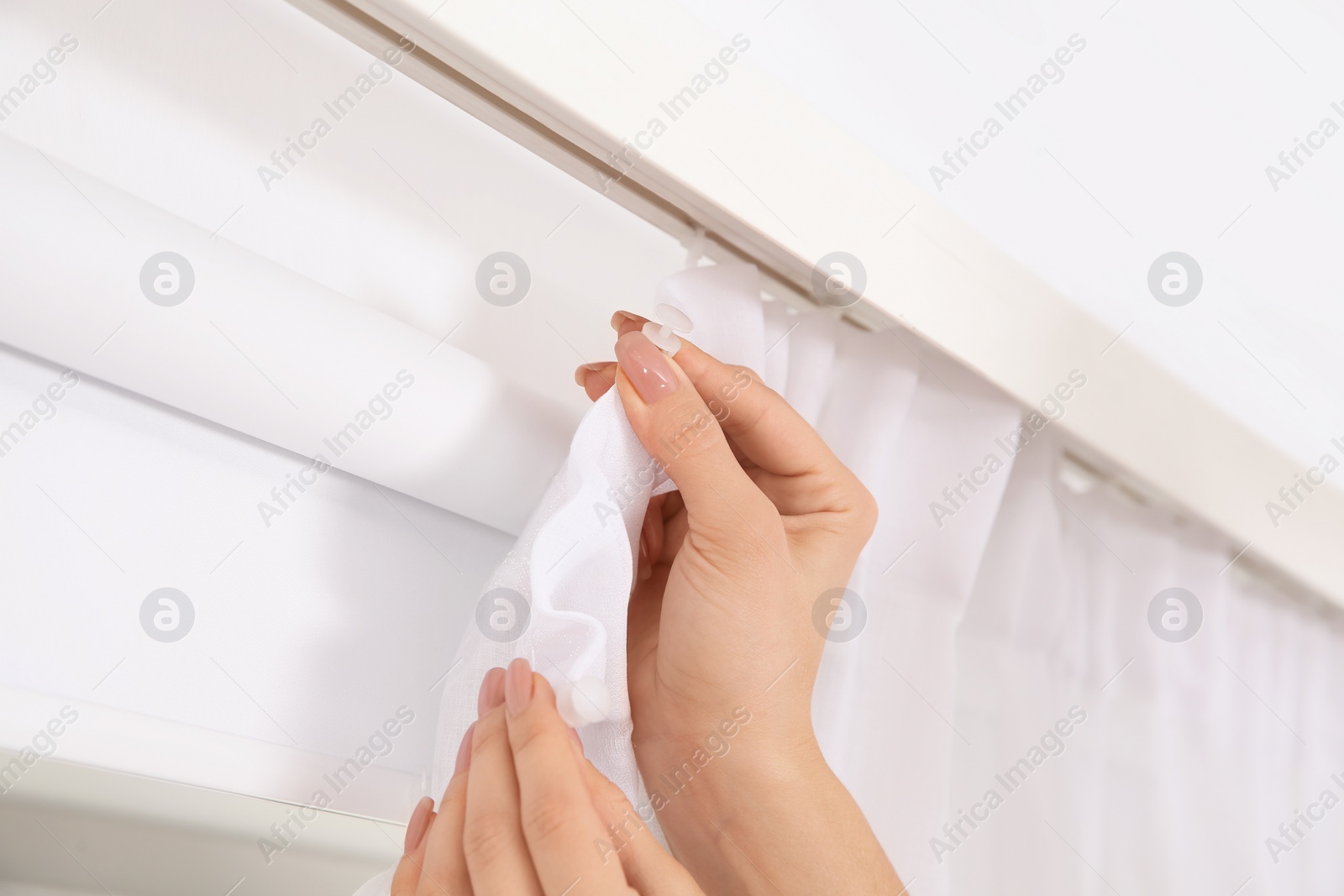 Photo of Woman hanging window curtain indoors, closeup. Interior decor element