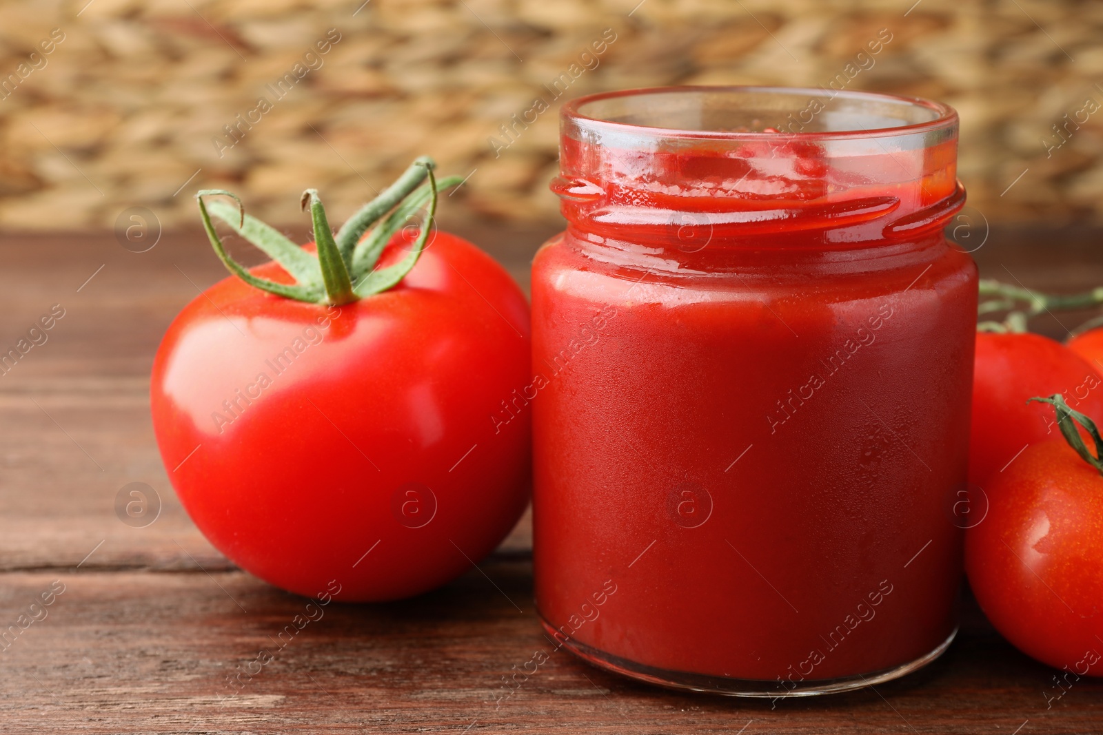 Photo of Jar of tasty ketchup and tomatoes on wooden table, closeup