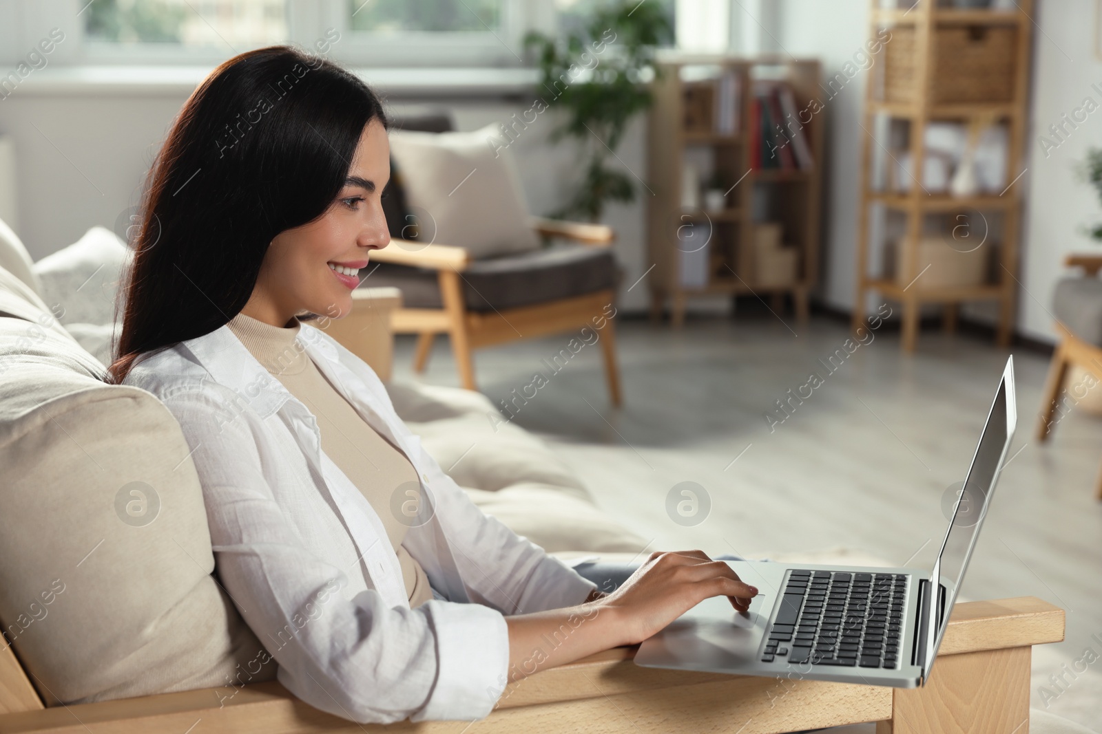 Photo of Young woman working with laptop on sofa at home