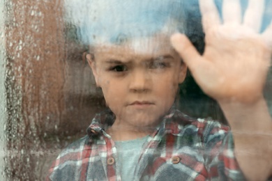 Photo of Cute little boy near window indoors. Rainy day