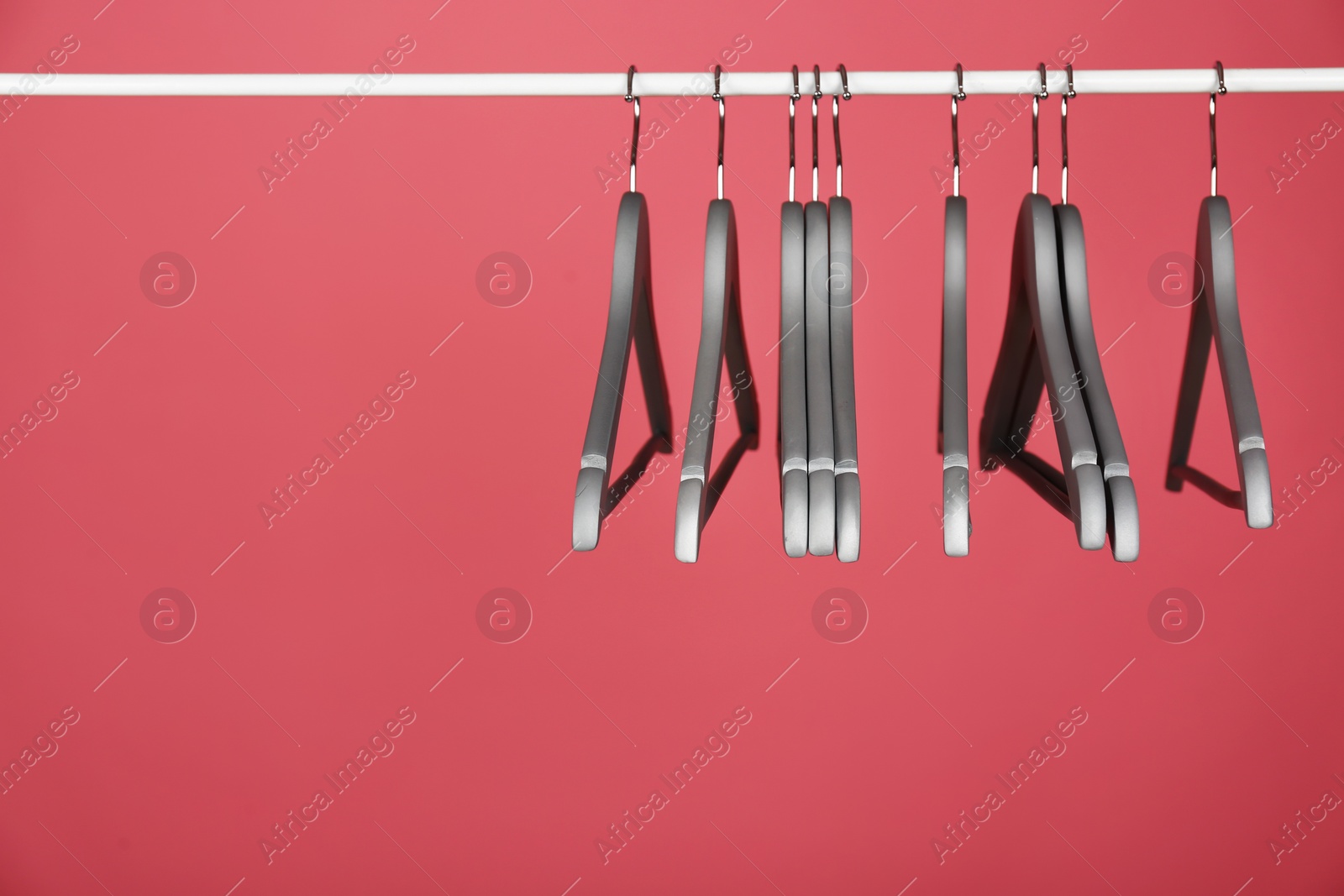 Photo of Empty clothes hangers on metal rail against color background. Space for text