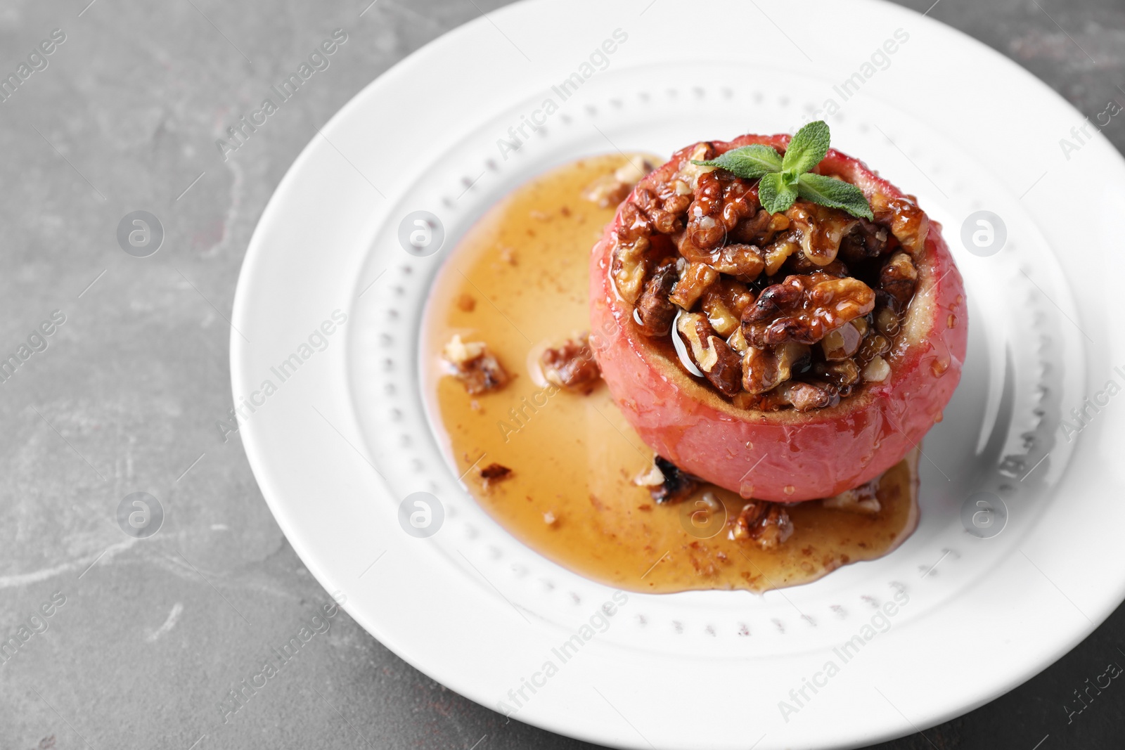 Photo of Tasty baked apple with nuts, honey and mint on gray table, closeup